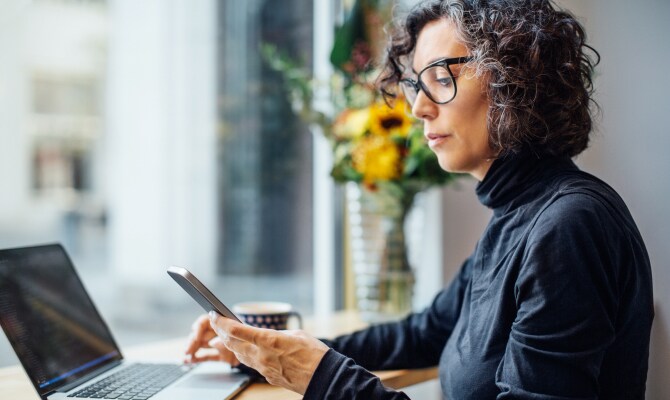 Mujer mirando un teléfono celular delante de una computadora portátil